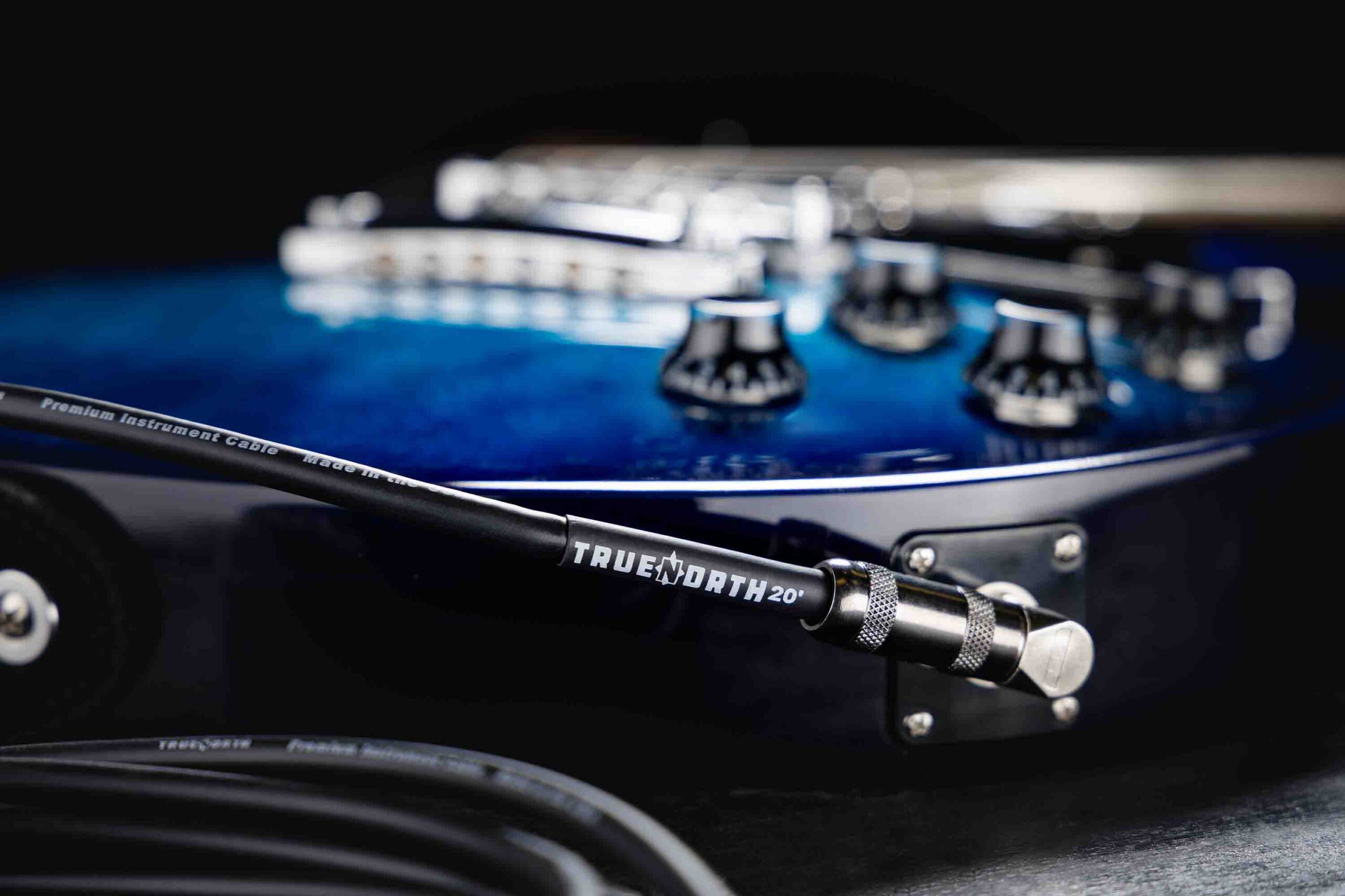 A True North instrument cable with a right-angle plug in front of a blue electric guitar